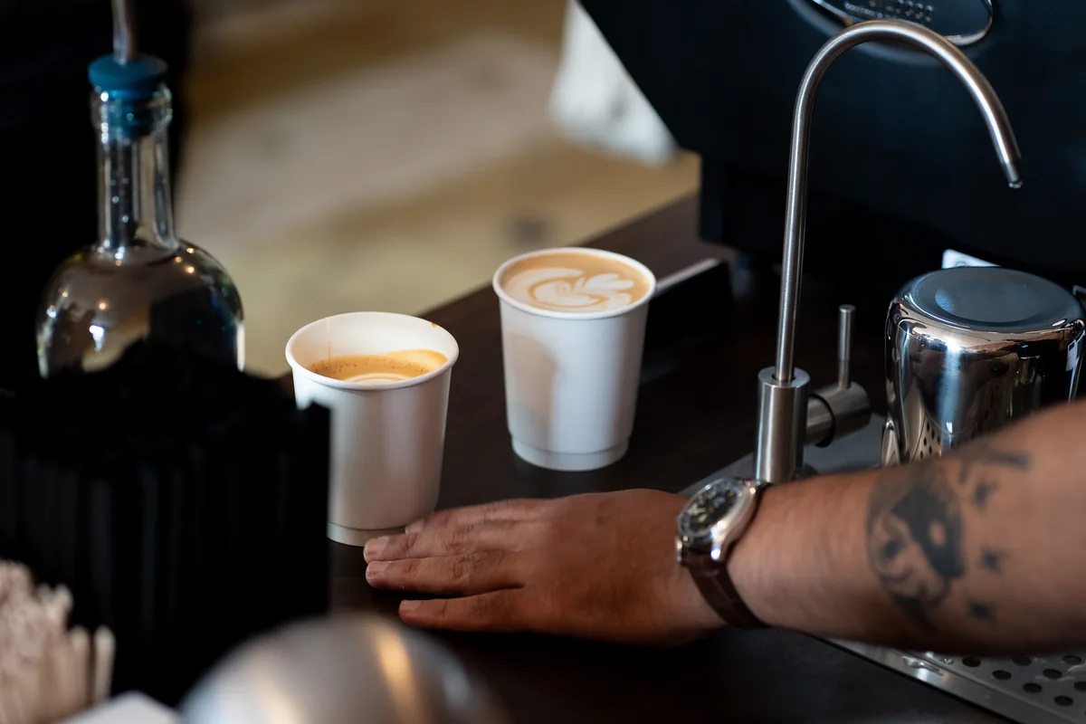 A cortado and a latte with latte art, handed across the ValdezNY espresso bar