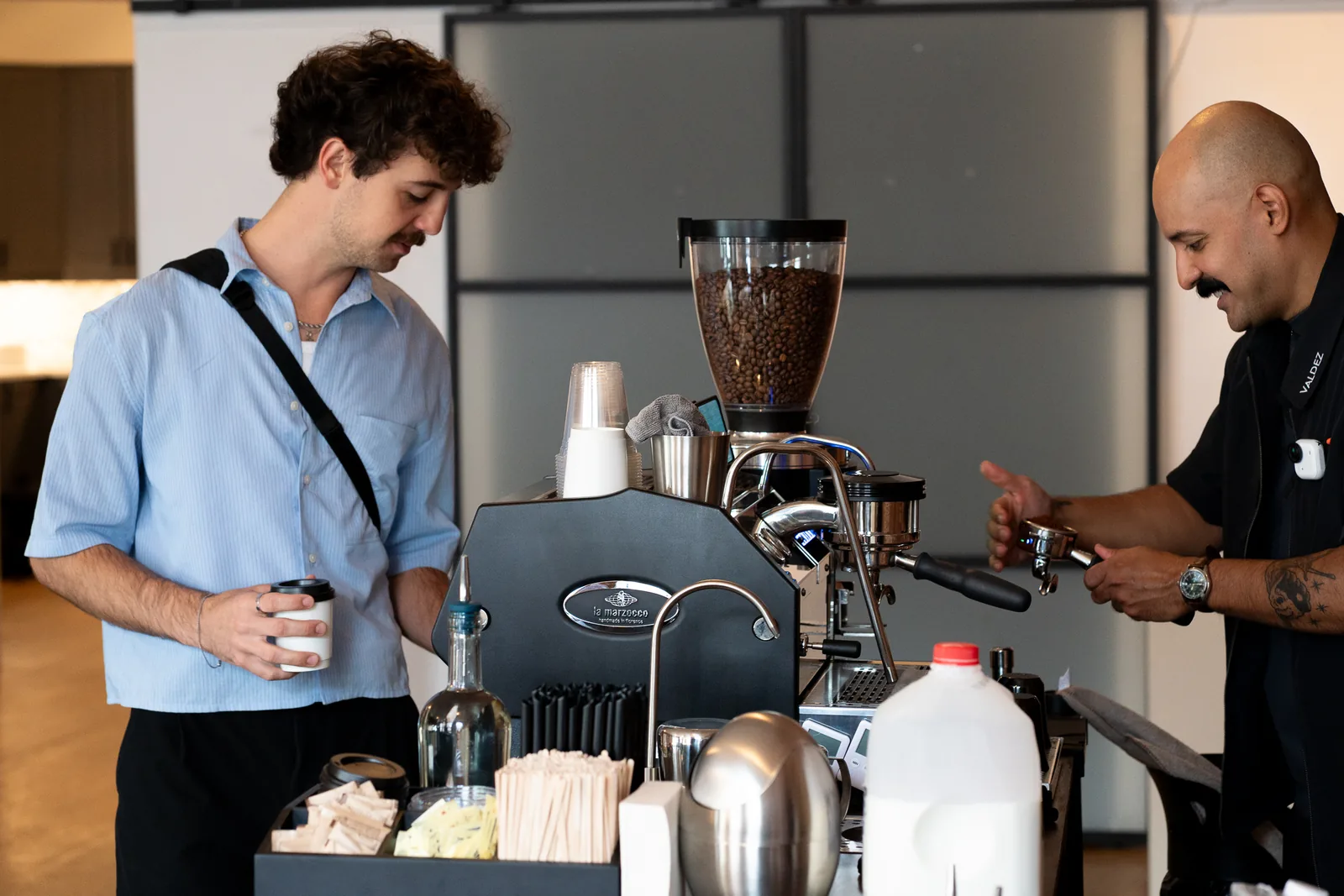 A guest holds his coffee as Michael Valdez prepares a shot on the La Marzocco espresso machine