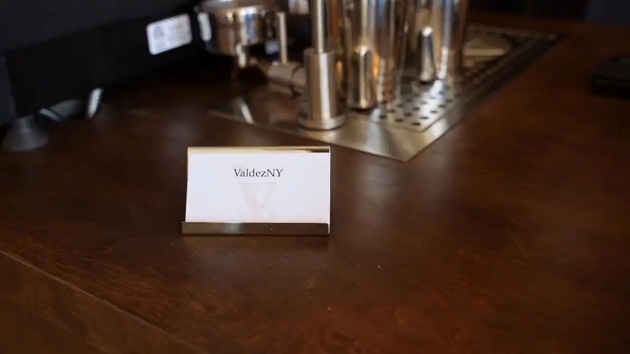 A latte set down on the bar beside a ValdezNY card