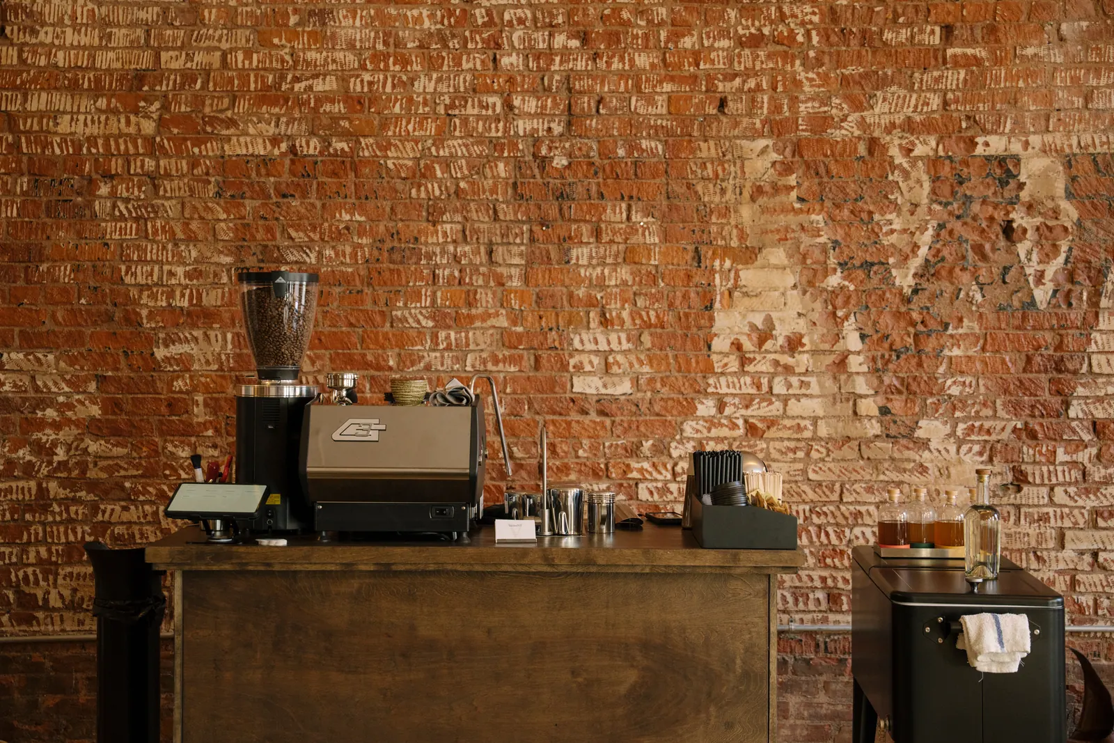 The ValdezNY espresso cart against exposed brick: La Marzocco GS3, grinder, ordering tablet, and syrup station